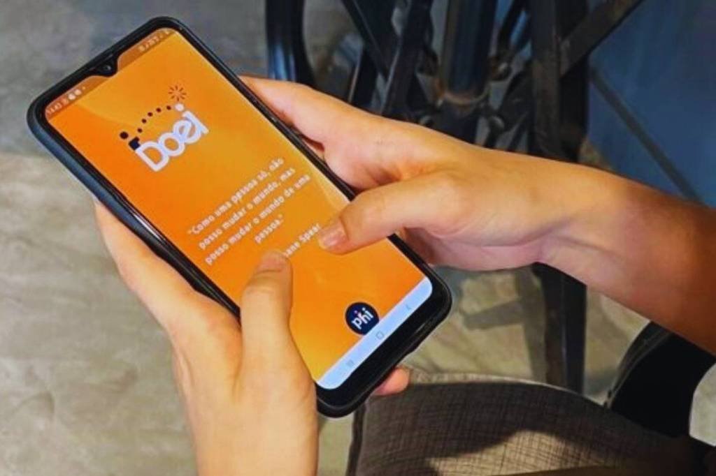 Uma pessoa está segurando um celular com a tela voltada para cima. O celular exibe o aplicativo