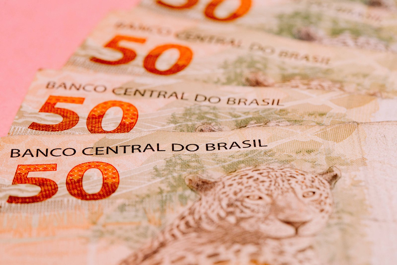 A imagem mostra várias notas de 50 reais do Brasil, com o texto
