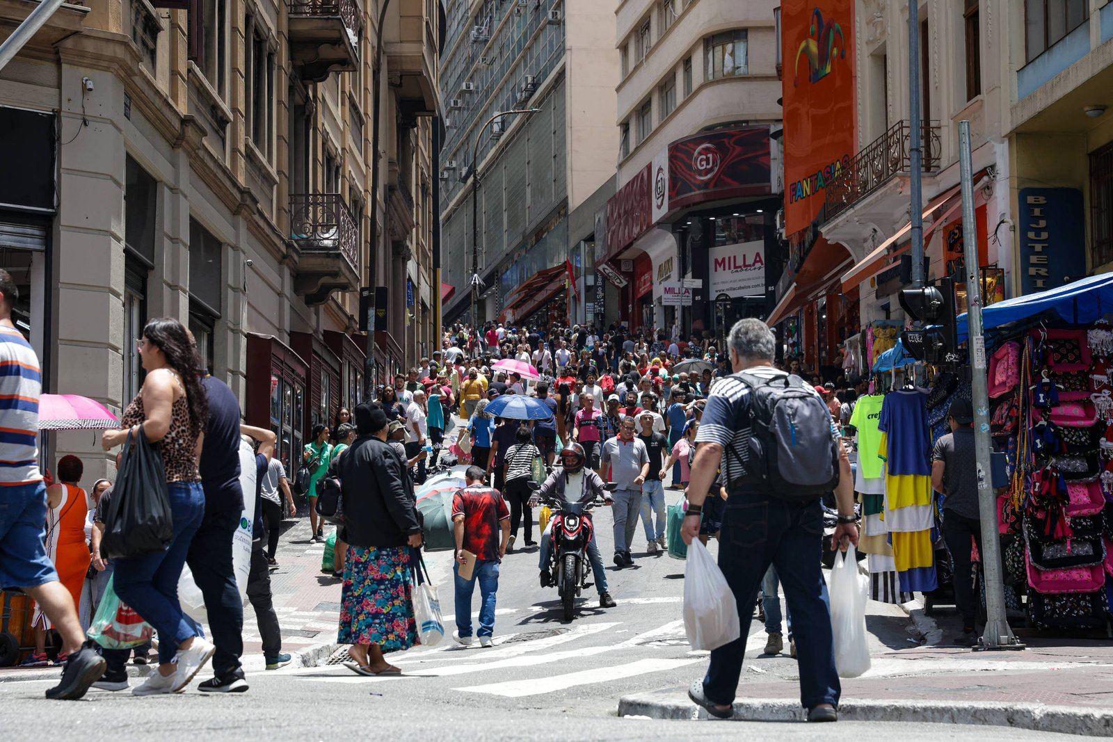 Imagem mostra pessoas caminhando na região da rua 25 de março, que abriga trabalhadores do comércio popular e consumidores em São Paulo.