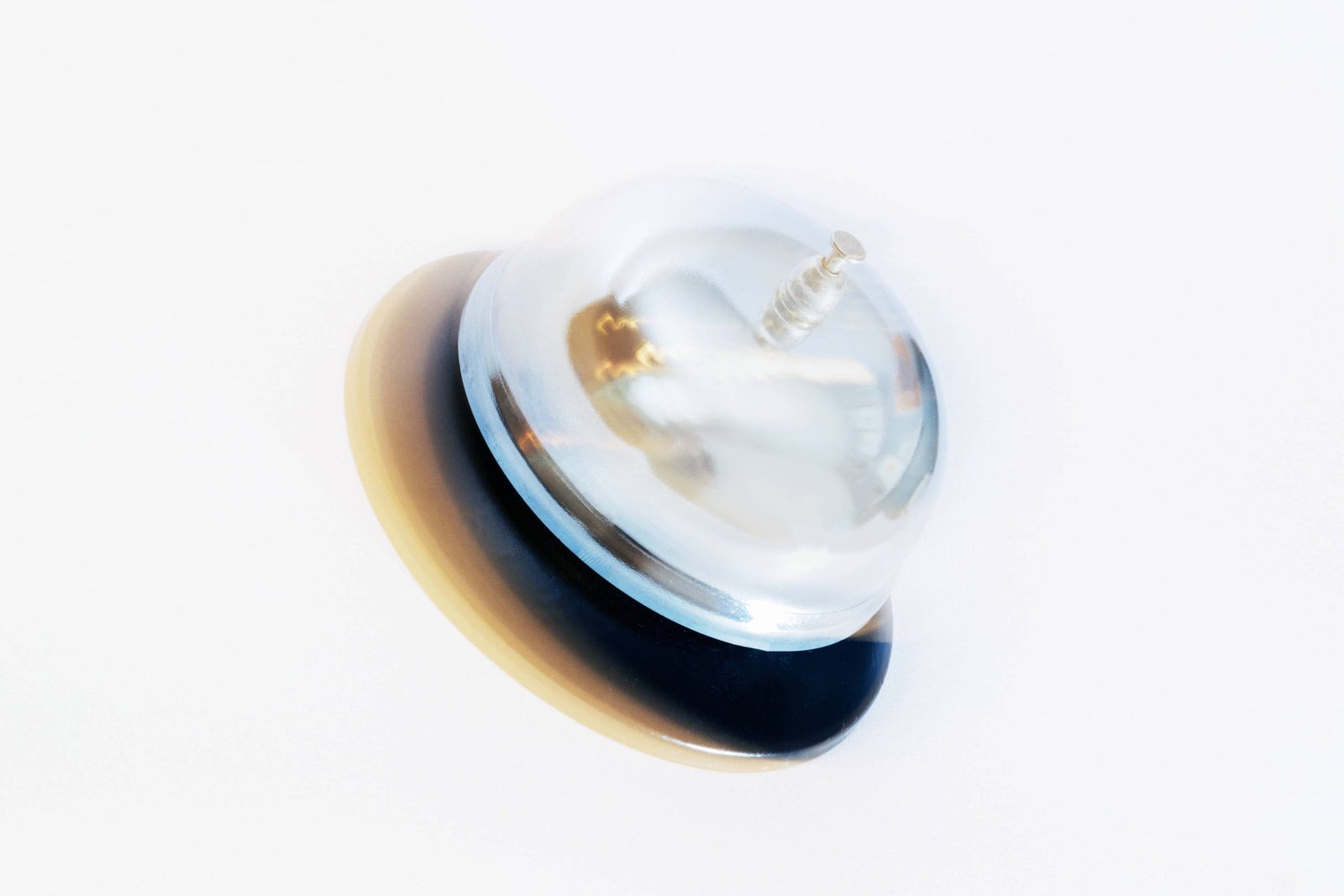 A imagem mostra um objeto transparente em forma de cúpula, com uma base arredondada de cor preta e uma parte inferior em tom claro. O objeto parece ser um tipo de botão ou interruptor, com um pequeno parafuso visível na parte superior.