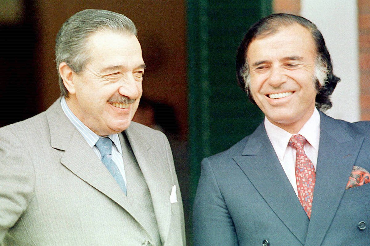 Retrato de dois homens, possivelmente políticos, com expressões amigáveis e vestimentas formais. Os dois homens são os principais sujeitos da imagem. Ambos possuem expressões amigáveis, sorrindo. Vestem ternos e gravatas.