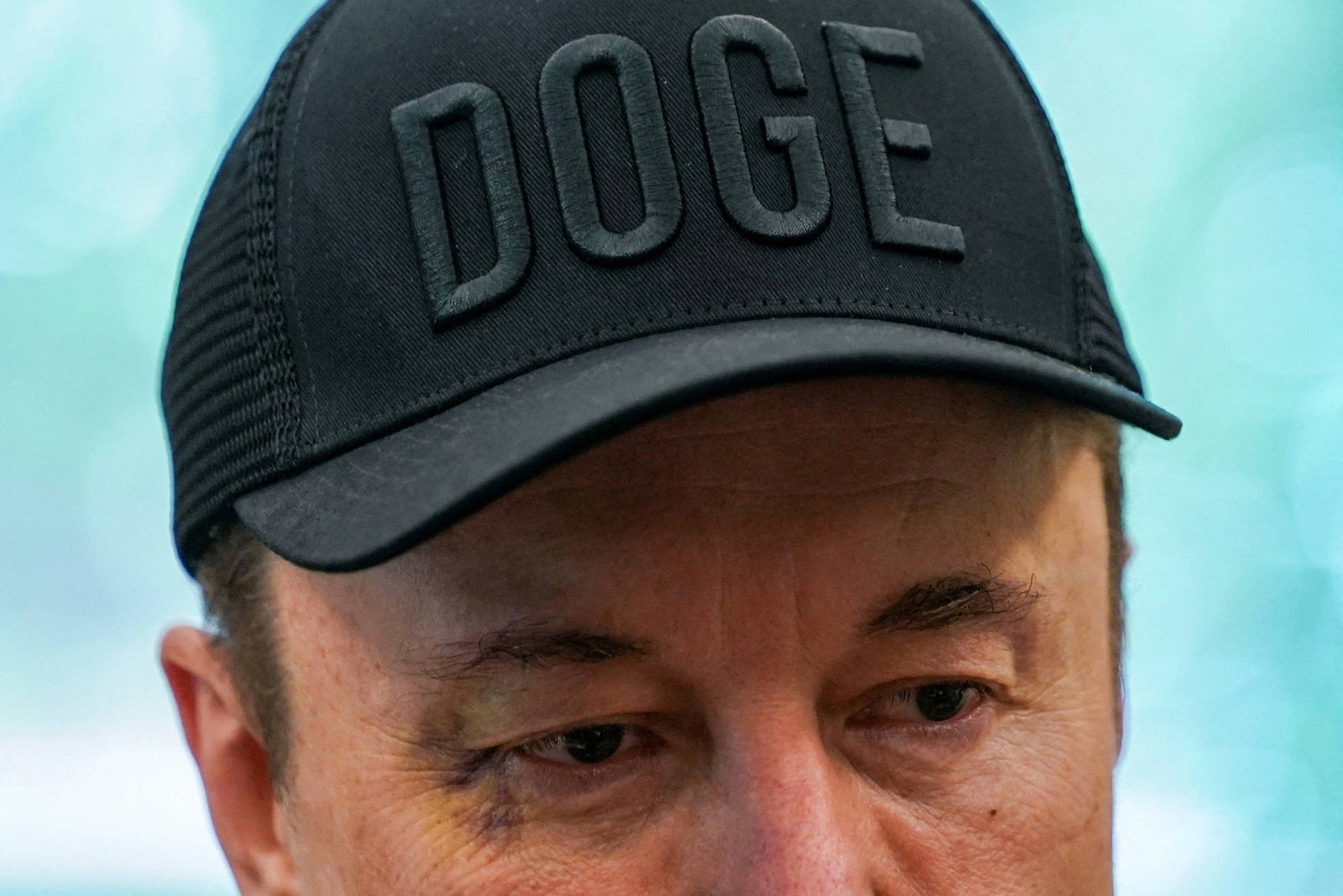 A imagem mostra um homem com um boné preto que tem a palavra