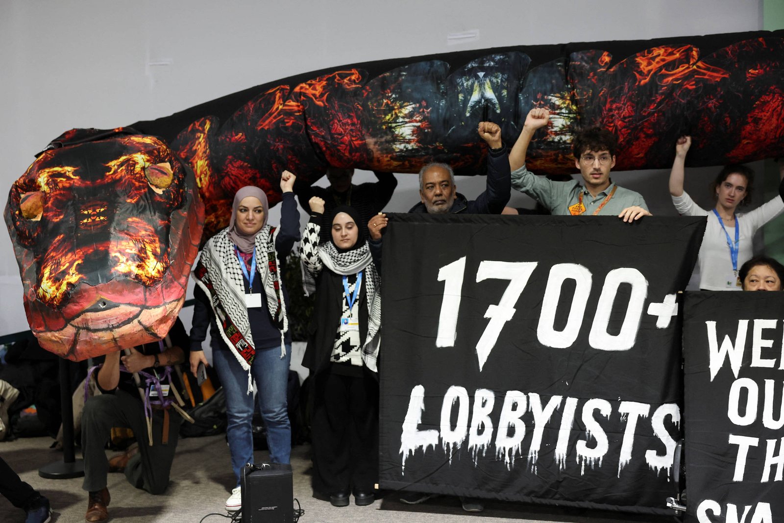 Pessoas com braço erguido ao lado de cobra inflável e de cartaz que diz