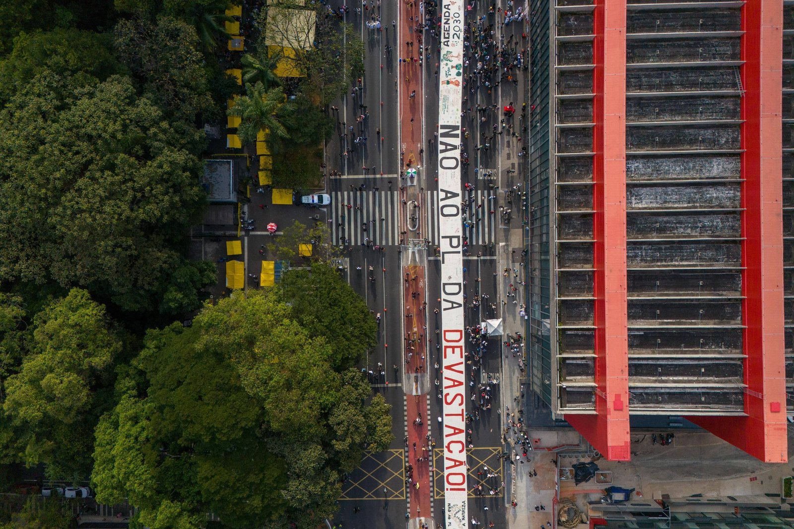 A imagem mostra uma grande faixa estendida sobre uma rua, com a inscrição