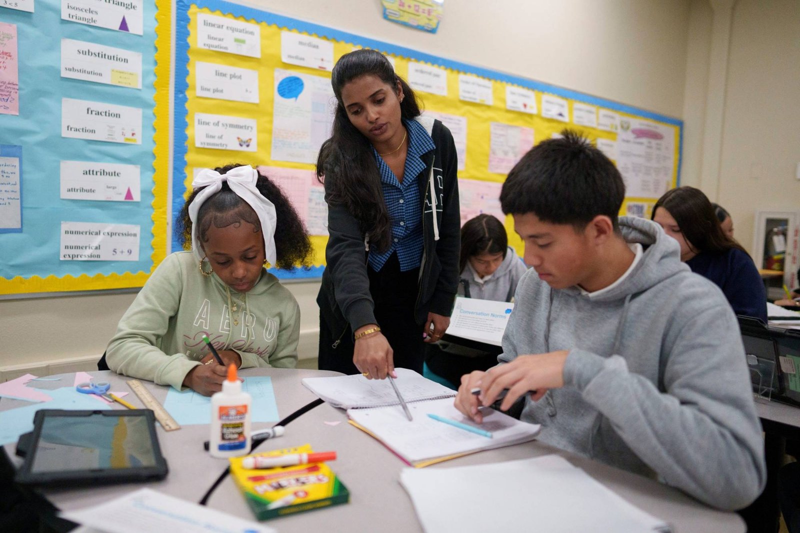 Teacher standing between two seated students in class.