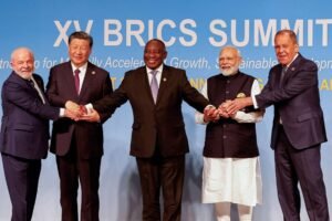 Cinco líderes do BRICS posam de mãos dadas em frente a um painel azul com o texto