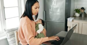Mother, baby and laptop in kitchen for remote work.