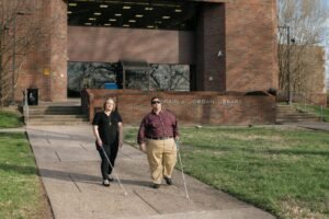 Two people who are blind are walking on the campus of West Virginia State University while holding canes.