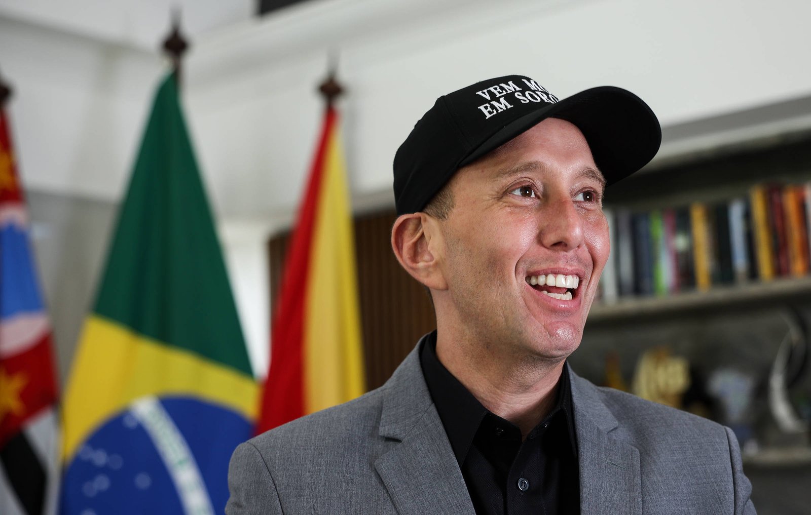 Um homem sorridente está usando um boné preto com a frase