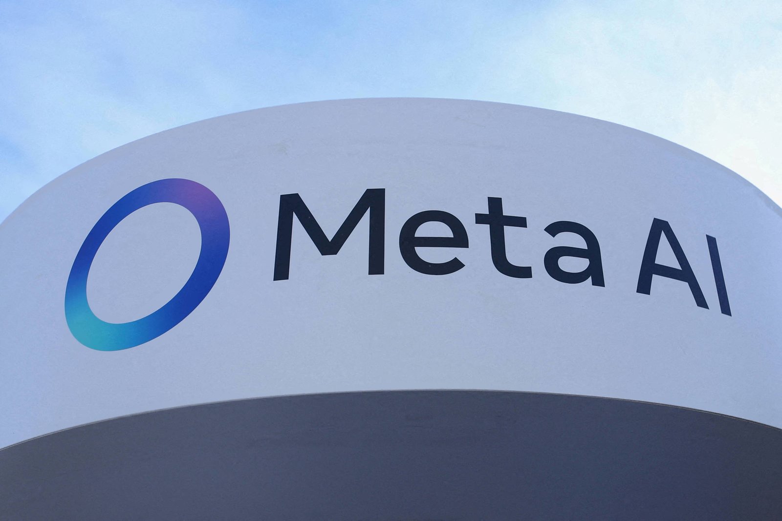 Logotipo da Meta AI em letras pretas sobre fundo branco curvo, com símbolo circular em degradê azul e roxo à esquerda, céu azul ao fundo.