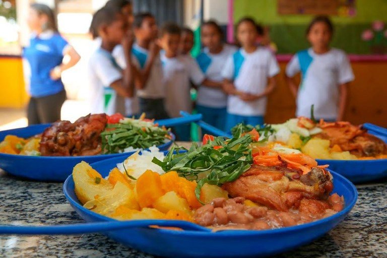 Pratos de comida da merenda escolar que serão servidos aos alunos, que estão aguardando para se alimentarem