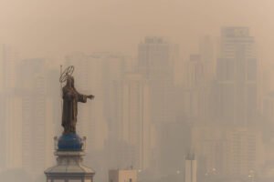 Imagem mostra estátua sobre torre de igreja com prédios ofuscados pela fumaça ao fundo