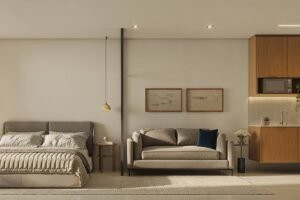 Imagem mostra o projeto de um apartamento. O ambiente interno tem cama de casal à esquerda, sofá cinza ao centro e cozinha compacta com armários de madeira à direita. Uma porta de vidro à esquerda permite entrada de luz natural e acesso a uma área com máquina de lavar.