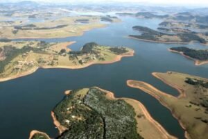 Reservatório de água com várias ilhas e penínsulas de terra cercadas por água. Vegetação verde cobre as áreas terrestres, e o céu claro é visível ao fundo.